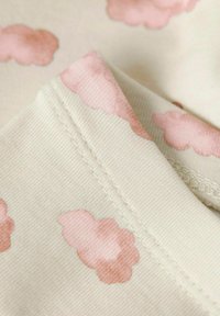 Baumwollstoff mit einem cremefarbenen Hintergrund und sanften rosa Wolkenmustern. Die Oberfläche ist leicht strukturiert mit sichtbaren Nähdetails.