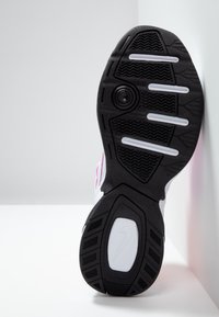 Semelle de sneaker Nike noire et blanche avec des motifs de grip texturés et des bandes de traction blanches horizontales sur fond blanc.