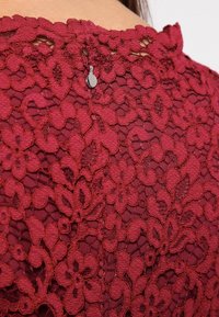 Kangas lace Burdeos, ikoni kukkakuviot, joissa on teksturoitu pinta ja pieni metallinen napitus niskassa.