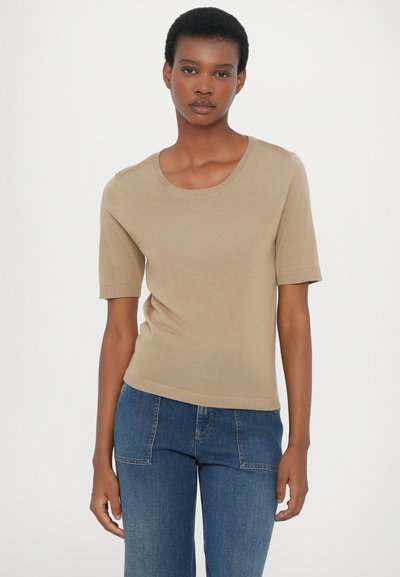 Beige, kortermet strikket topp med rund hals; har ribbestruktur på ermer og kant, kombinert med blå denimjeans.