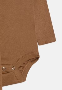 Body bébé à manches longues de couleur marron uni, fabriqué en textile doux avec des boutons-pression au fond et une texture lisse.