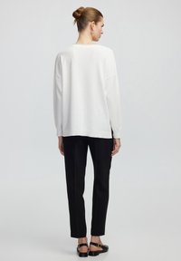 Bílý svetr, volný střih, žebrované manžety a lem. Spárováno s černými elegantními kalhotami a černými plochými sandály se zlatými kovovými detaily.