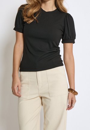 Haut noir côtelé avec manches courtes bouffantes, encolure ronde et silhouette ajustée. Associé à un pantalon taille haute de couleur claire.