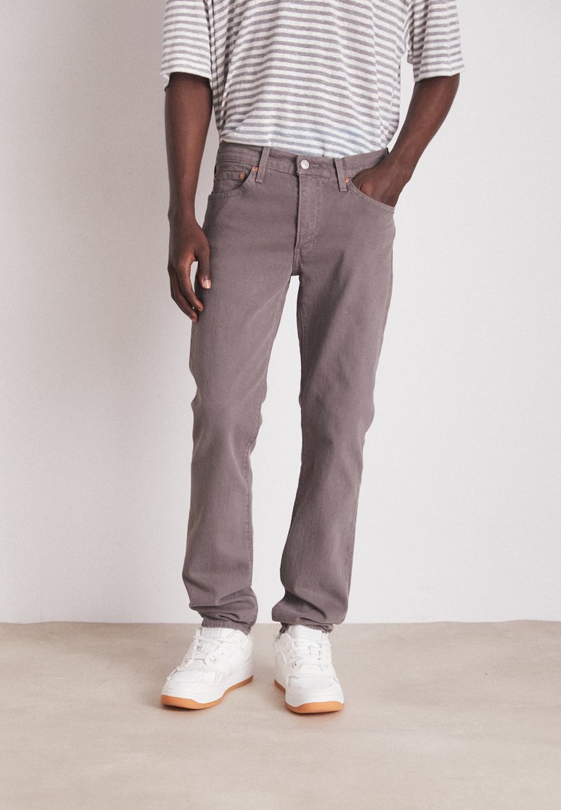 Šedé bavlněné džíny s rovnými nohavicemi, doplněné světle šedým a bílým pruhovaným tričkem a bílými teniskami s oranžovými detaily.