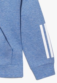 Modrá sportovní mikina vyrobená z texturované látky, s klokaní kapsou, ribbed manžetami a třemi bílými vertikálními pruhy na rukávu.