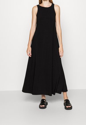 Černé bezramínkové maxi šaty z lehkého materiálu s volným střihem. V kombinaci s plochými černými sandály s otevřenou špičkou.