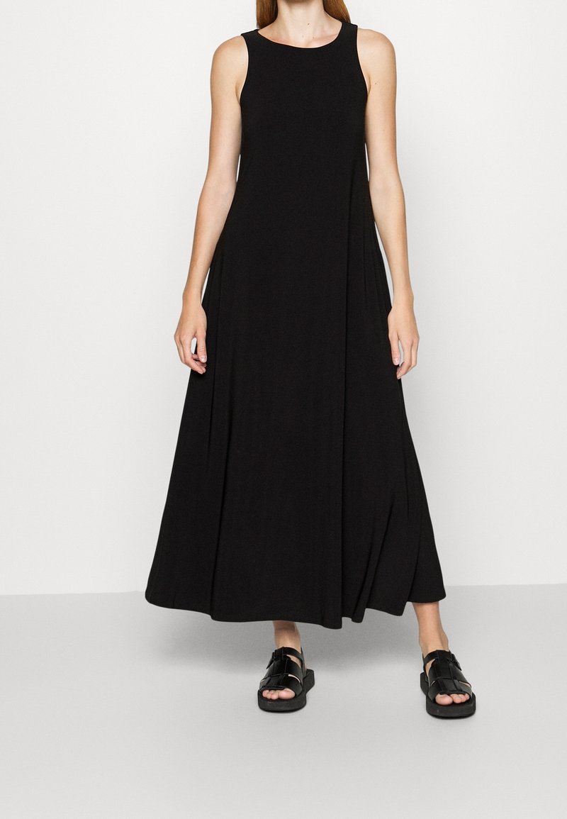 Svart ärmlös maxiklänning i lätt tyg med en svängig silhuett. Matchad med platta svarta sandaler med öppen tå-design.