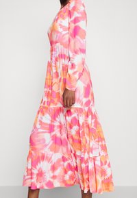 Robe à manches longues tie-dye aux nuances de rose et d'orange, dotée d'une jupe à volants et d'une coupe décontractée. Confectionnée dans un tissu doux et léger.