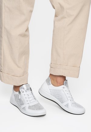 Weiße und silberne Low-Top-Sneaker mit seitlichen Reißverschlüssen, getragen zu beigen Cordhose, deren Saum umgeschlagen ist.