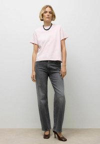 Lichtroze cropped t-shirt met korte mouwen, gecombineerd met hoge taille grijze rechte jeans en bruine hakken. Eenvoudige zwarte kralenketting.