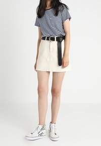 Pruhované tmavě modré a bílé tričko, krémová džínová sukně s roztrhaným lemem, černý opasek a bílé tenisky s vysokým svrškem a kostkovaným vzorem.