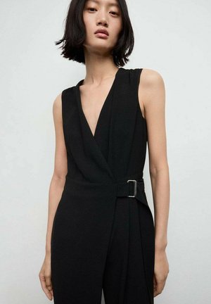 Mono negro sin mangas con un profundo escote en V, diseño envolvente y hebilla plateada en la cintura. Fabricado en una tela suave, presenta un corte entallado.