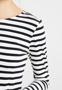 Zbliżenie na osobę w czarno-białą pionową w paski koszulę z długim rękawem na jednolitym jasnym tle.