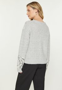Maglione grigio a maglia con maniche lunghe e ampie, con dettagli di paillettes sui polsini, texture morbida e vestibilità rilassata. Realizzato in materiale confortevole.