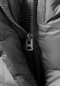 Čierna vypchávkovaná bunda s plastovým zipsom, zobrazujúca textúrovanú tkaninu a suchý zips na vnútornej strane, zdôrazňujúca teplo a funkčnosť uzáveru.