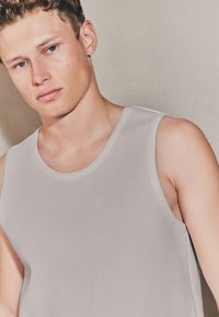 Lichtgrijze tanktop met een geribbelde textuur en een ronde halslijn, voorzien van brede armsgaten en een aansluitend ontwerp.
