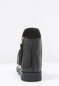 Bottine en cuir noir à fermeture éclair, avec des détails en frange et une semelle texturée. Fini lisse avec des accents de couture sur les côtés.