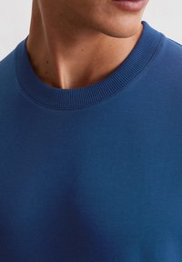 Niebieski bawełniany sweter z okrągłym dekoltem, z detalami w rib, o gładkiej teksturze, z naciskiem na zbliżenie szycia i jakość tkaniny.