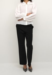 White long-sleeve blouse with ruffled collar, paired with black tailored trousers and sparkly pointed-toe heels. Smooth fabric and structured fit.