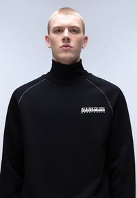 Felpa nera con colletto alto e aderente. Presenta un logo bianco sul petto sinistro e cuciture sottili lungo le maniche raglan. Texture liscia.