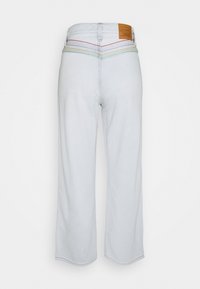 Vaaleansiniset korkeavyötäröiset denimhousut, joissa on leveät lahkeet, sateenkaaren väriset takakappaleen ompeleet ja ruskea nahkainen Levi's-logotarra.