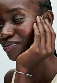 Silver bracelet with small beads and a pearl accent on a dark-skinned person’s wrist, featuring neutral nail polish and smooth skin texture.