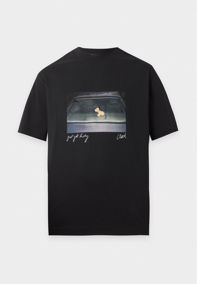 T-shirt noir avec une photo du tableau de bord d'une voiture présentant une petite figurine de chien, et un texte manuscrit indiquant "Just get lucky" et "Clawed."