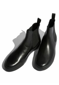 Botas de tobillo negras con un exterior de cuero suave, paneles laterales elásticos y una suela de goma plana. Diseño minimalista con tiradores.