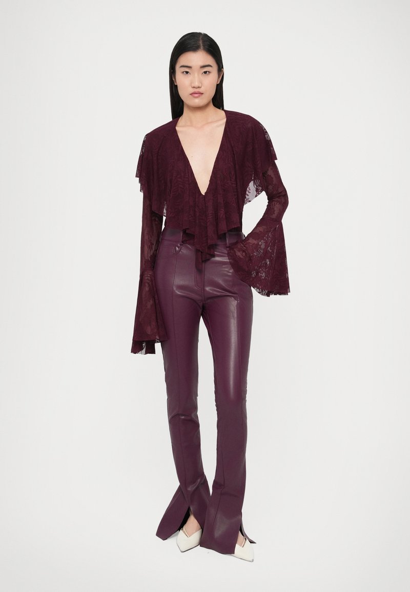 Bordeauxrode kanten top met gelaagde ruches en een diepe V-hals, gecombineerd met hooggetailleerde, glanzende bordeauxrode leren broek met zijopeningen.
