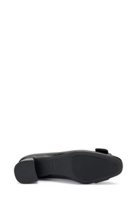 Zapato de cuero negro con suela plana y punta redondeada. Presenta una superficie lisa y un acabado mate sutil, acentuado por un pequeño detalle de lazo.