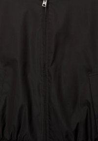 Sort zip-jakke lavet af glat, mat stof. Har to sidelommer og elastiske manchetter i kanten for et tætsiddende look.