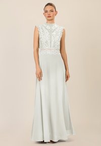 Lang, lichtgroene jurk met een hoge kant bodice, gegolfde randen en een vloeiende rok. Ontworpen met een aansluitende taille en een mouwloze silhouette.