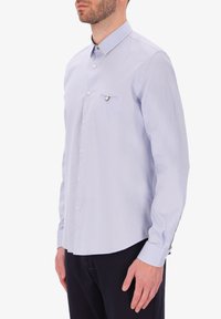 Camicia a maniche lunghe azzurro chiaro con colletto button-down, taschino sul petto e bottoni bianchi, realizzata in un tessuto liscio.