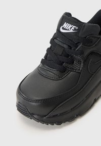 Sapatilha Nike preta com parte superior em couro liso, biqueira reforçada, acabamentos texturizados e atacadores redondos pretos. Logotipo na lingueta.