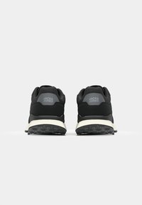 Black athletic shoes with a smooth textile upper, featuring a cushioned sole, a grey brand logo on the heel, and textured rubber outsole.