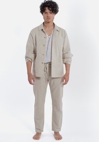 Camicia di lino beige con colletto e bottoni, abbinata a pantaloni di lino coordinati. Design semplice, vestibilità comoda, tasche visibili sulla camicia.