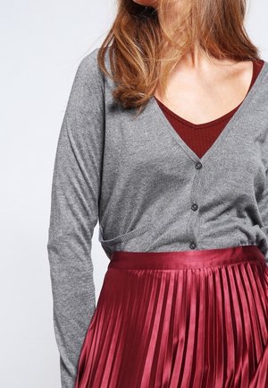 Cardigan grigio con scollo a V e bottoni, abbinato a una gonna di raso bordeaux plissettata. L'outfit presenta texture morbide e sottili sovrapposizioni.
