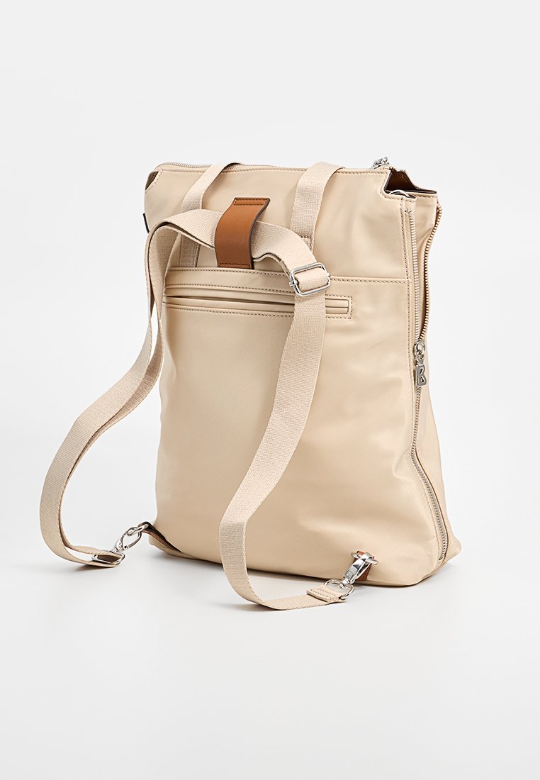 Beige Rucksack aus synthetischem Material, mit einem Reißverschluss, verstellbaren Trägern und einem braunen Lederakzent an der Oberseite.