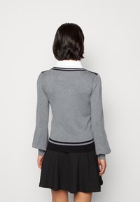 Pull en tricot gris avec un col blanc, doté de rayures noires au col et à la taille, associé à une jupe évasée noire.