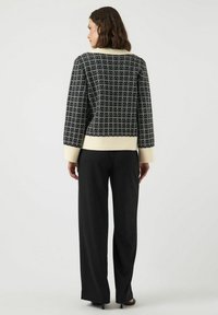 Svart och vit mönstrad stickad tröja med ribbat gräddfärgat nederkant och ärmar, kombinerad med lösa svarta byxor.