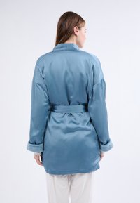 Robe en satin bleu clair avec une ceinture à la taille, dotée de manches larges et de poignets doux et texturés. Finition lisse avec une coupe décontractée.