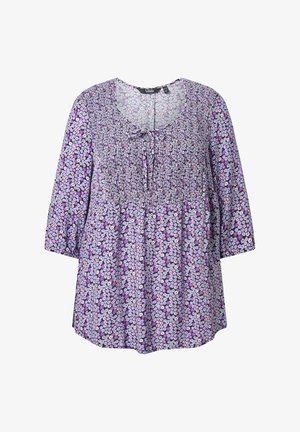 Blusa floreale viola con maniche tre quarti, scollo arricciato e dettaglio a fiocco, caratterizzata da un tessuto testurizzato con tonalità di lavanda e fiori bianchi.