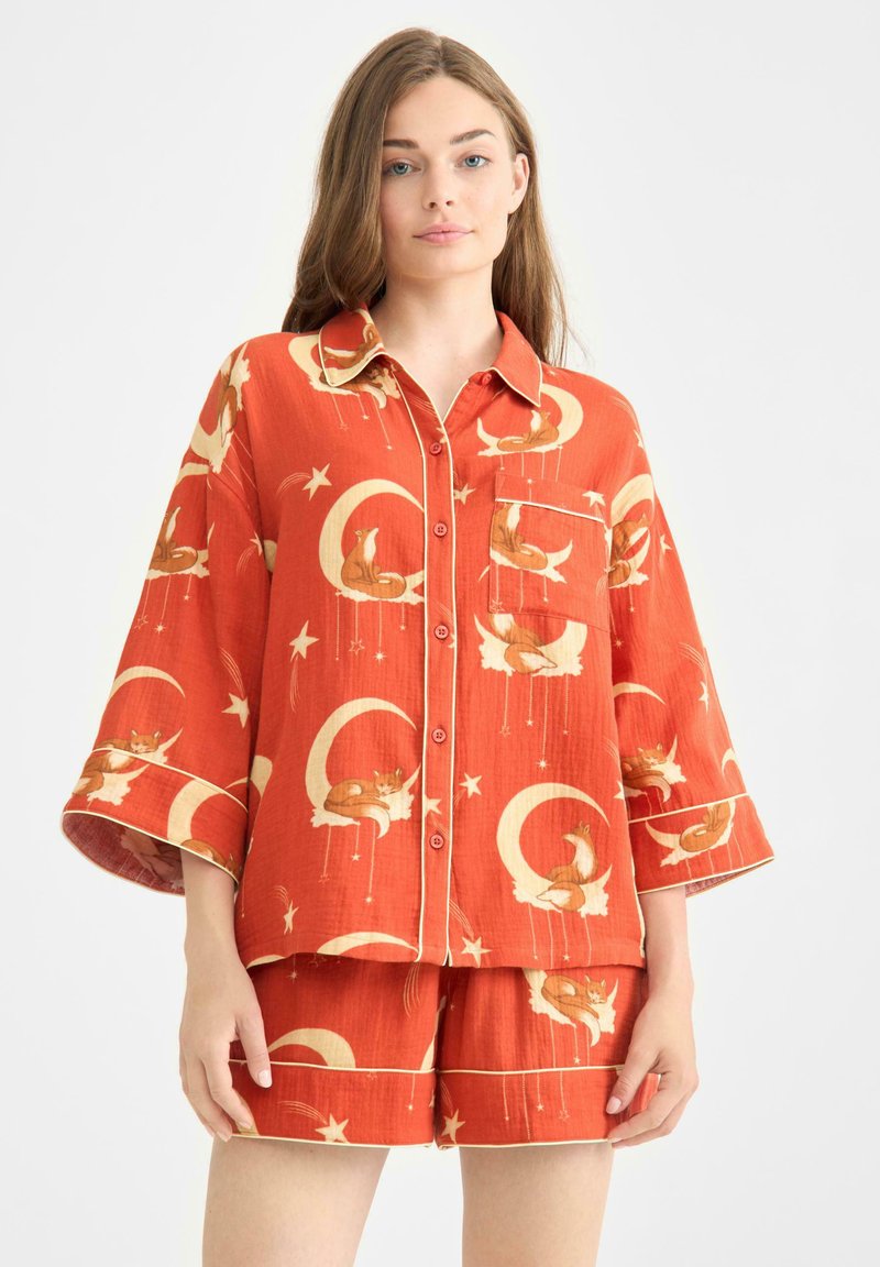 Orange tvådelat pyjamasset med kortärmad skjorta och shorts. Tryckt med rävar, månar och stjärnor; mjukt, lätt tyg.