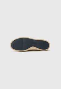 Semelle de chaussure avec un fond en caoutchouc beige, présentant une zone texturée bleu foncé et des rainures pour l'adhérence. Design simple et épuré sans motifs.