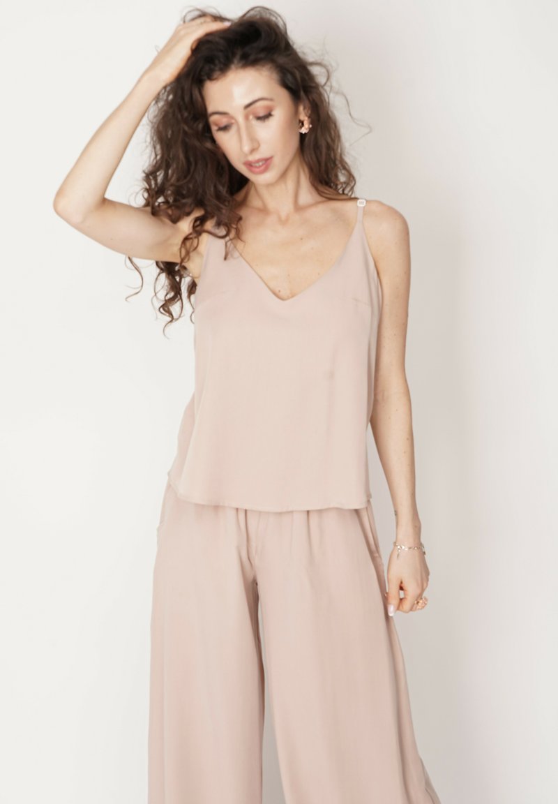 Jasnoróżowa, zwiewna bluzka na ramiączkach z dekoltem w kształcie litery V oraz cienkimi ramiączkami. Gładka faktura, minimalistyczny design. Łączona z dopasowanymi spodniami o szerokich nogawkach.