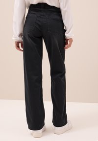 Zwarte hoge taille broek met wijd pijpen, subtiele textuur, vijf zakken en een nette afwerking. Gecombineerd met witte sneakers.