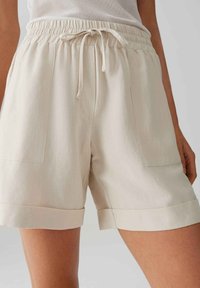 Beige katoenen shorts met een elastische tailleband en trekkoord, voorzien van twee voorkruiken en een opgerolde zoom. Soepele, lichte textuur.