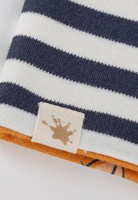 Striped fabric in navy and white, featuring an orange hem and a label with a brown splash design. Soft knit texture.