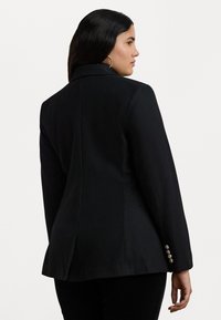 Črni krojeni blazer s strukturo. Ima usnjeni ovratnik, enojno zapiranje na gumb, zračen hrbet in kovinske gumbe na manšetah.