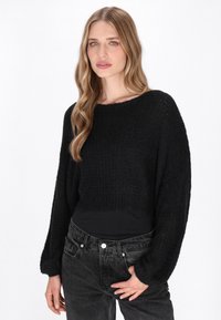 Pulover scurt negru, tricotat, cu un model texturat, guler larg tip barcă și mâneci lungi, asortat cu blugi din denim închis.